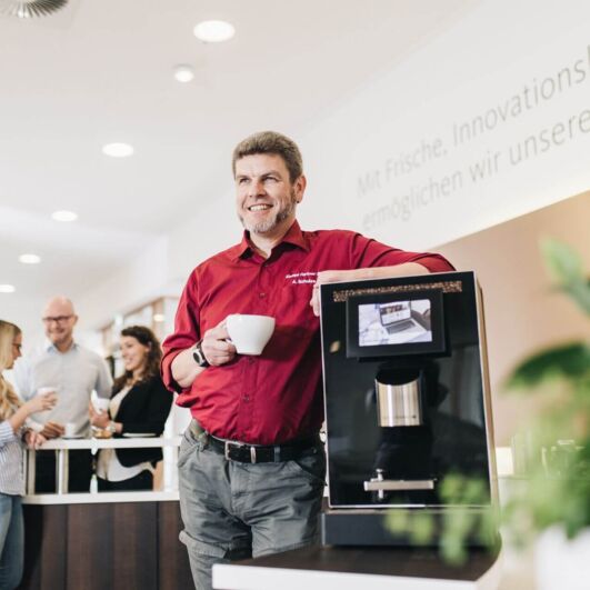 Service employee standing next to a coffee machine and drinking coffee.